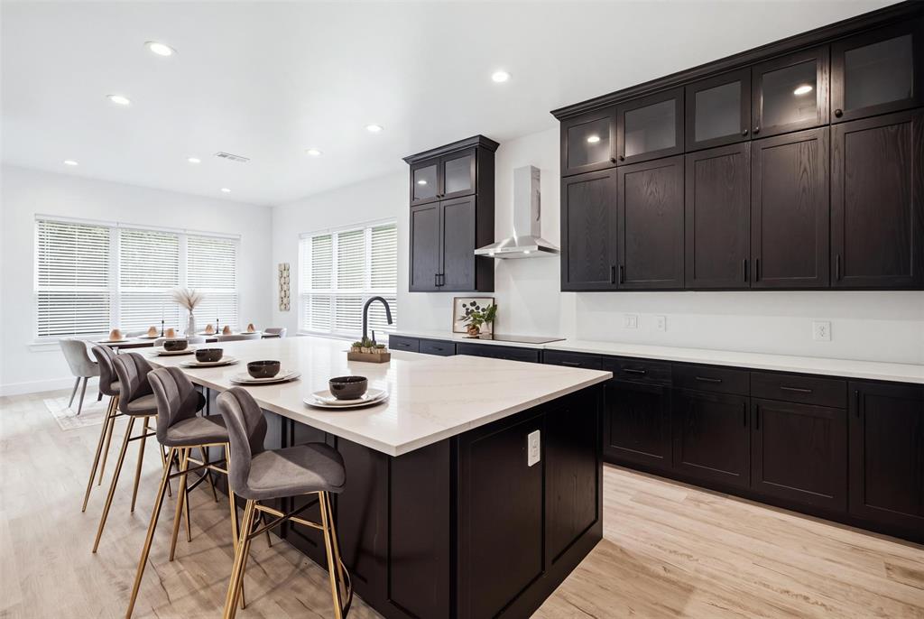 Kitchen featuring dark wood-finish cabinetry with glass-front uppers, a central island, stone-finish countertops, recessed lighting, and a stainless steel range hood
