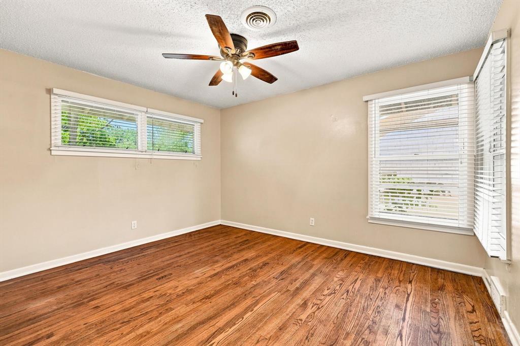 Room featuring wood-finish flooring, multiple windows with horizontal blinds, and a multi-blade ceiling fan with integrated lighting