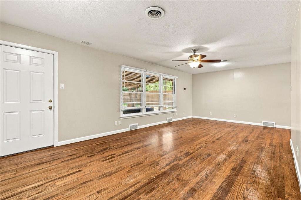 Room featuring wood-finish flooring, a multi-pane window with blinds, a white six-panel entry door, and a ceiling-mounted light fixture with a fan