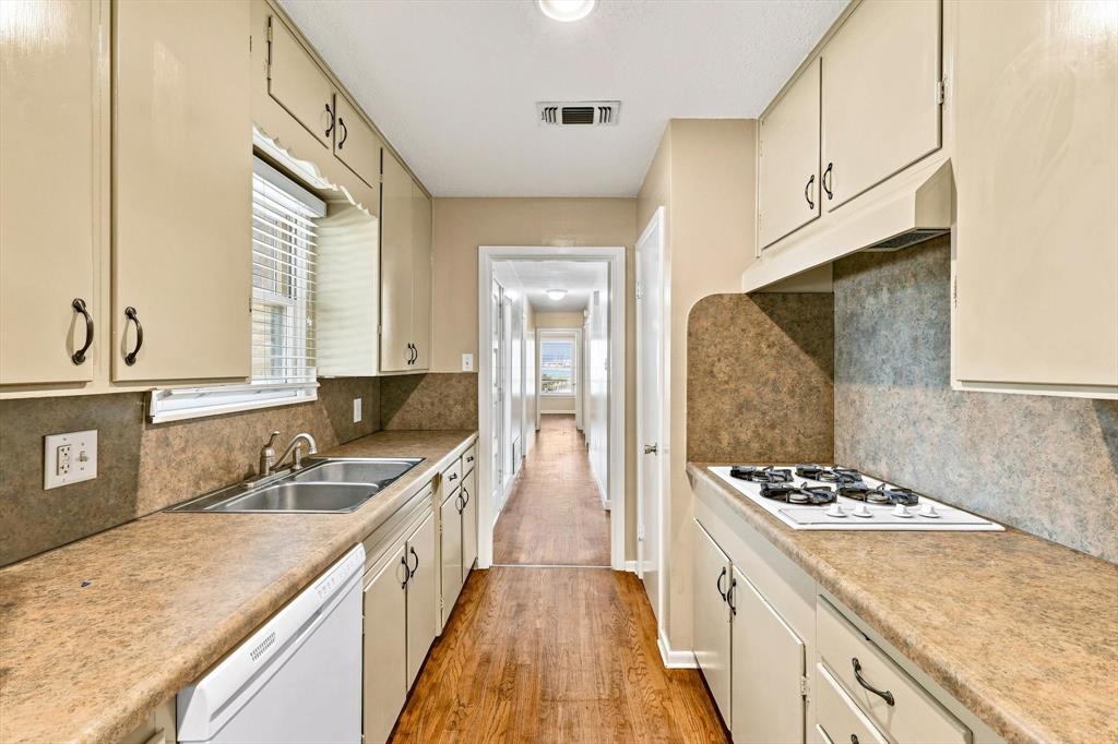 Galley kitchen featuring light cabinetry, solid-surface countertops with matching backsplash, a stainless steel dual-basin sink, and a built-in gas cooktop