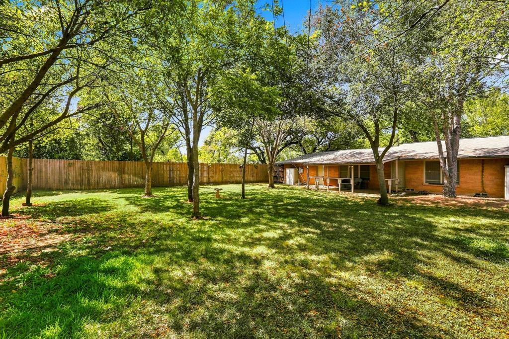 Expansive backyard featuring a lawn, mature trees, wood privacy fencing, and a covered patio
