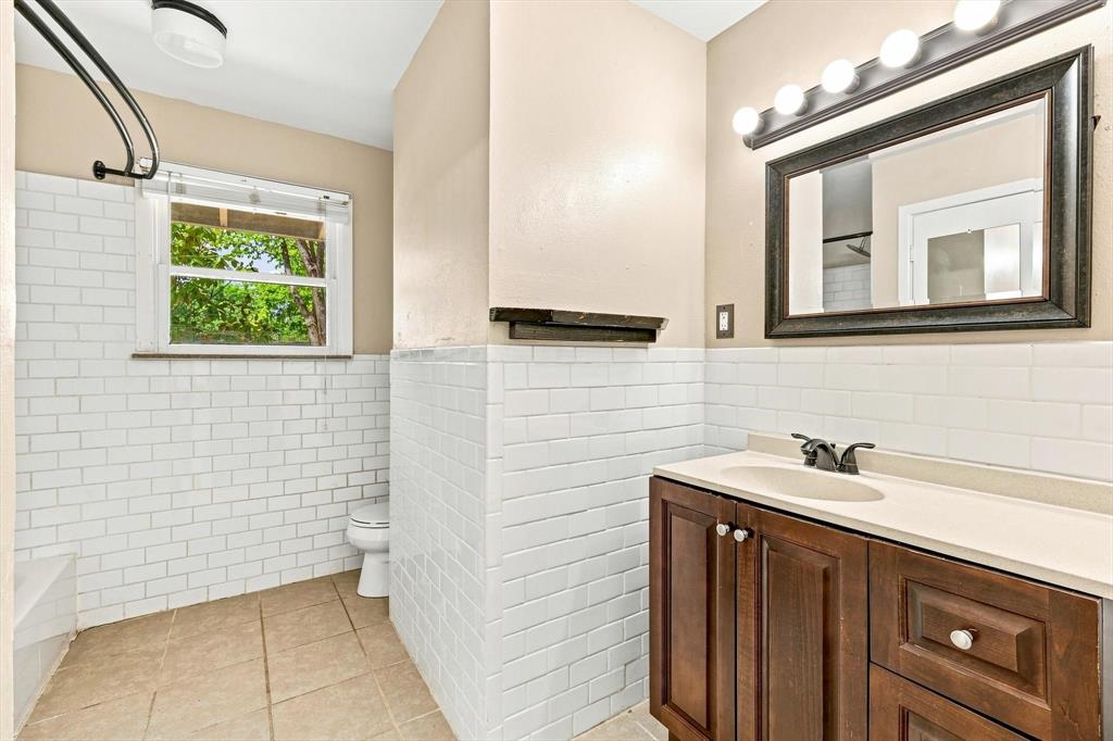 Bathroom featuring white subway tile wainscoting, dark-finish wood cabinetry, integrated countertop with oval sink, and a framed vanity mirror with integrated light fixture