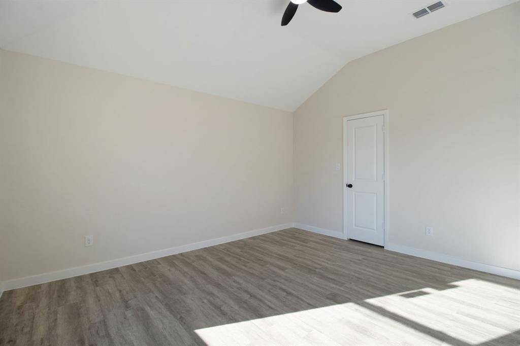 Vaulted ceiling, wood-finish flooring, white paneled door with black hardware, neutral wall paint, and ceiling fan