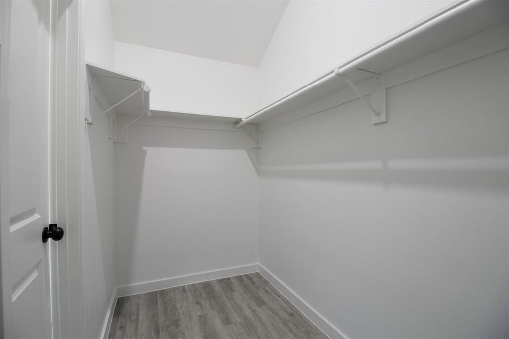 Walk-in closet with wood-finish flooring, white walls, built-in shelving, and a hanging rod