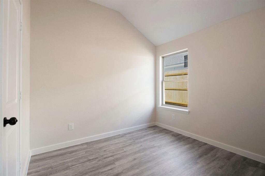 Vaulted ceiling with wood-finish flooring, a single window, and a white door with black hardware