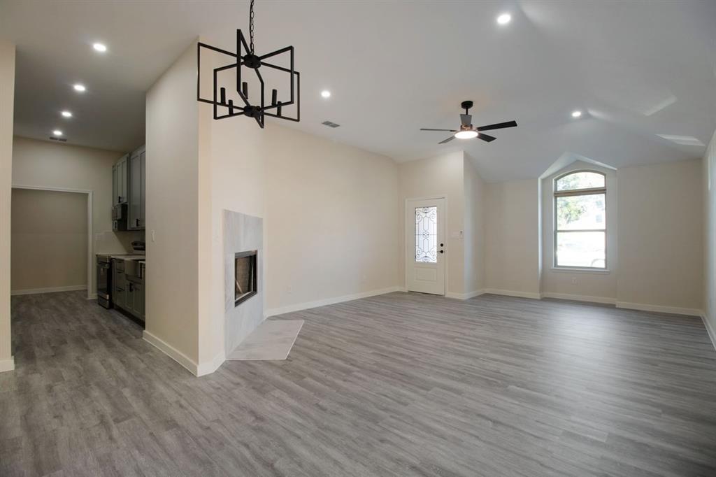 Spacious room featuring wood-finish flooring, a contemporary fireplace with a light-toned surround, a modern chandelier, and recessed lighting