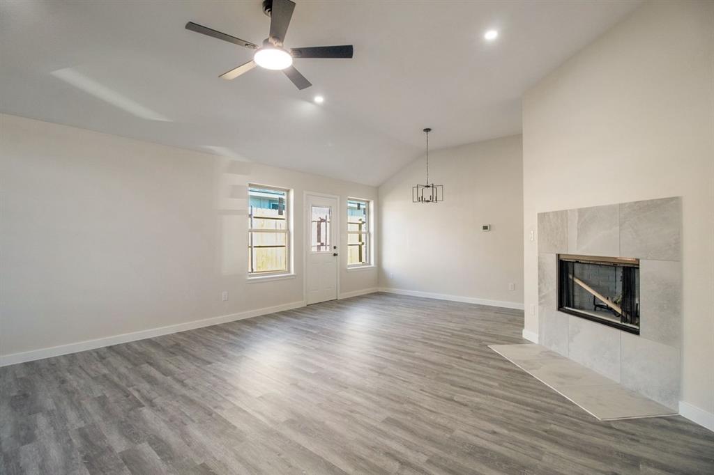 Vaulted ceiling, wood-finish flooring, white walls, built-in fireplace with tile surround, and an exterior door with integrated windows