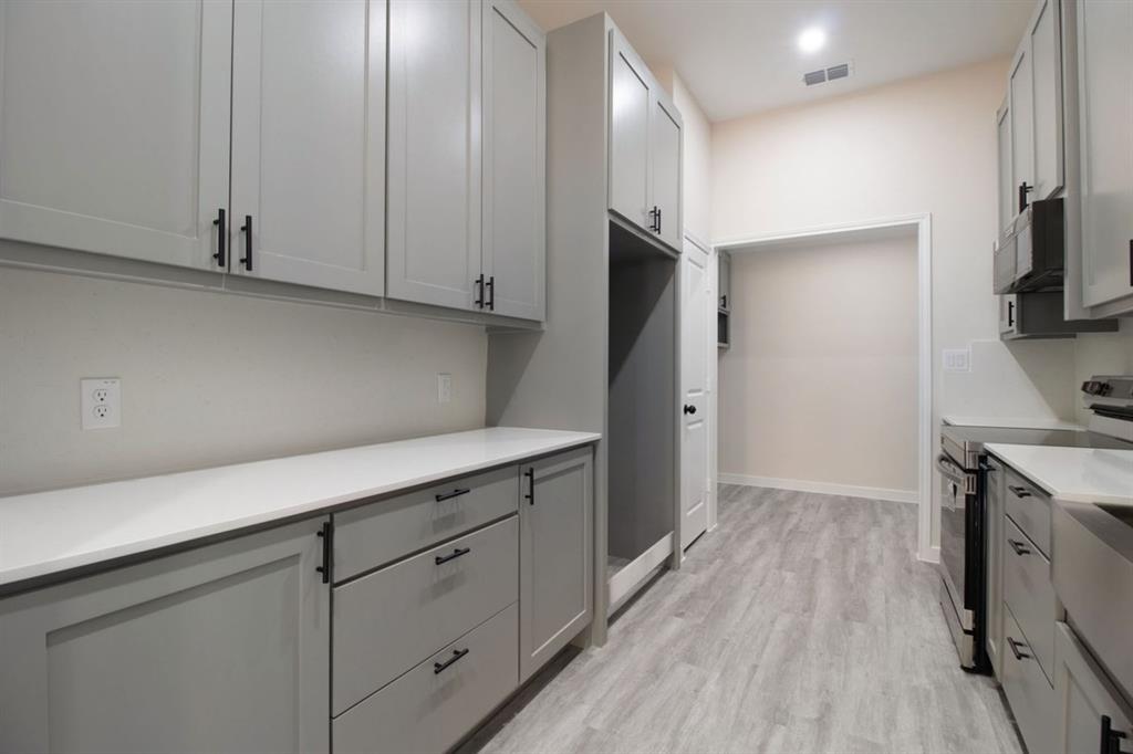 Galley kitchen featuring shaker-style cabinetry with matte black hardware, light-toned countertops, and wood-finish flooring