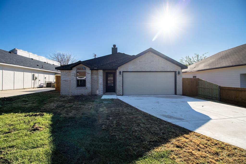 Light-colored brick exterior with dark trim, an attached two-car garage, concrete driveway, and a wood privacy fence