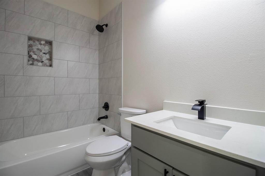 Bathtub with tiled surround and integrated niche, matte black fixtures, vanity with integrated sink, and white countertop