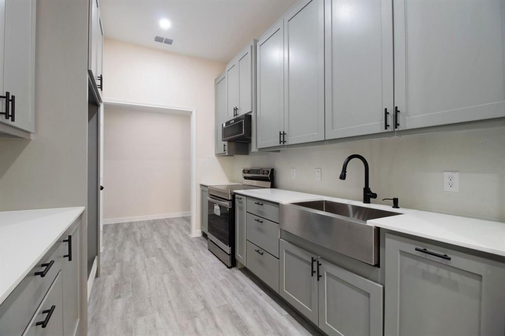 Wood-finish flooring, white countertops, stainless steel farmhouse sink, matte black faucet, and modern gray cabinetry