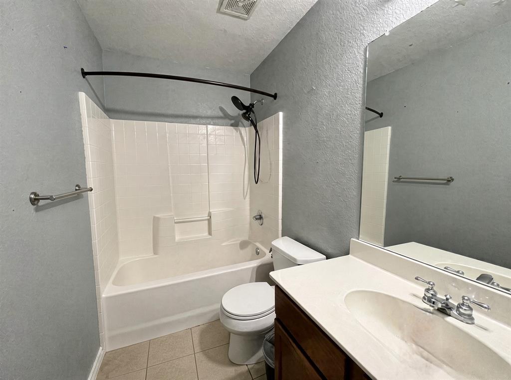Bathroom featuring a vanity with an integrated sink, white composite tub and shower surround, wall-mounted mirror, and ceramic tile flooring