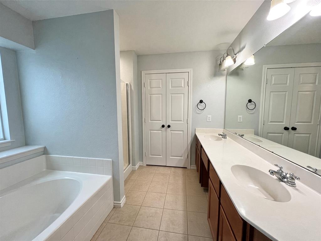 Dual vanity with a stone-surface countertop, porcelain sinks, tile flooring, soaking tub with tile surround, and expansive wall-mounted mirror Dual vanity with a stone-surface countertop, porcelain sinks, tile flooring, soaking tub with tile surround, and expansive wall-mounted mirror