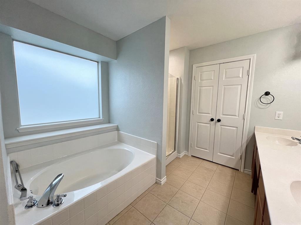 Bathroom featuring a tile-surround soaking tub, frosted window, double-door closet, tiled flooring, and dual-sink vanity