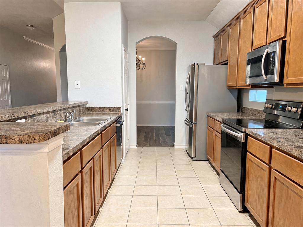 Kitchen featuring wood cabinetry, stainless steel appliances, laminate countertops, and ceramic tile flooring Kitchen featuring wood cabinetry, stainless steel appliances, laminate countertops, and ceramic tile flooring
