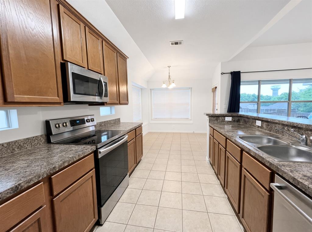 Kitchen featuring wood cabinetry, stone-patterned countertops, stainless steel appliances, and tile flooring Kitchen featuring wood cabinetry, stone-patterned countertops, stainless steel appliances, and tile flooring