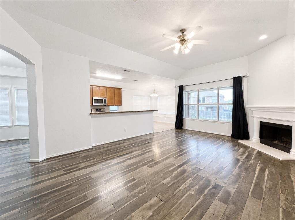 Living area featuring wood-finish flooring, vaulted ceilings, a fireplace with a white mantel, a ceiling fan, and a breakfast bar