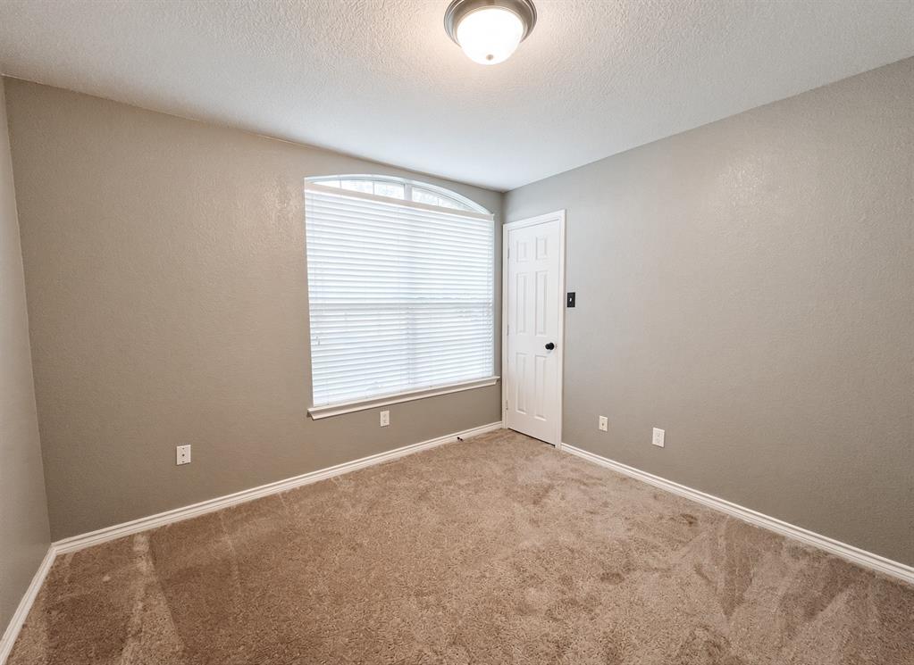 Neutral interior space featuring carpeted flooring, a six-panel door, and an arched window with horizontal blinds