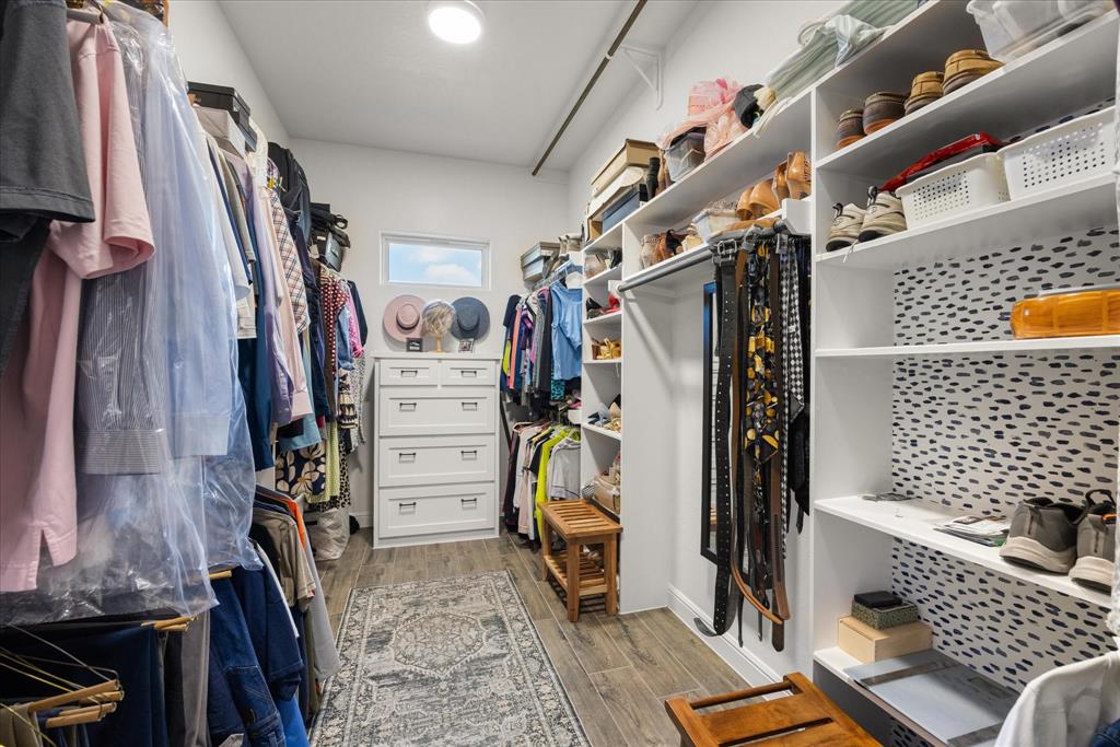Walk-in closet featuring white built-in shelving, integrated hanging rods, wood-finish flooring, and a single transom window