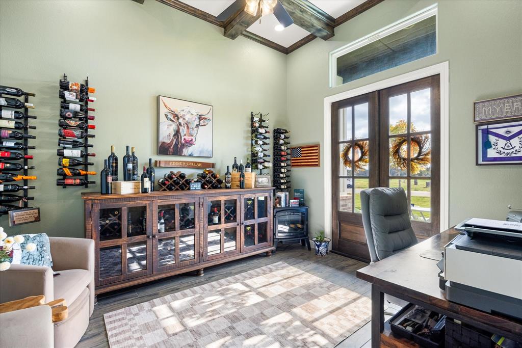 Vaulted ceiling with exposed wood beams, stained wood-finish double entry doors with transom window, built-in wooden cabinetry with glass paneling, and wall-mounted metal bottle storage racks