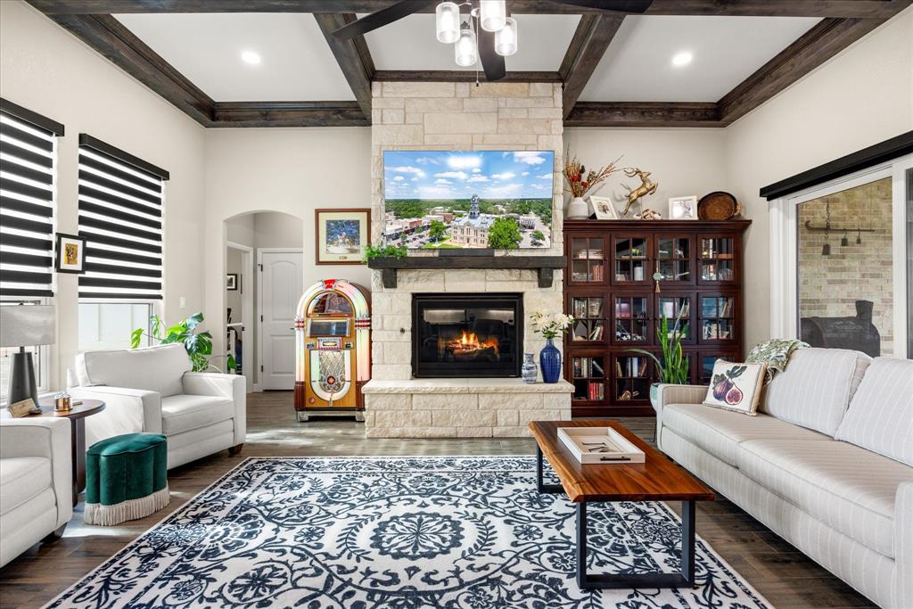 Living room featuring a floor-to-ceiling stone fireplace with a thick timber mantel, dark wood coffered ceiling beams, wood-finish flooring, and built-in dark wood cabinetry