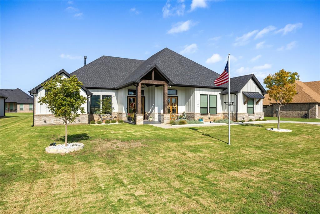 Modern farmhouse exterior featuring vertical white siding, stone veneer base, dark metal roof accents, and a covered entryway with timber-frame details