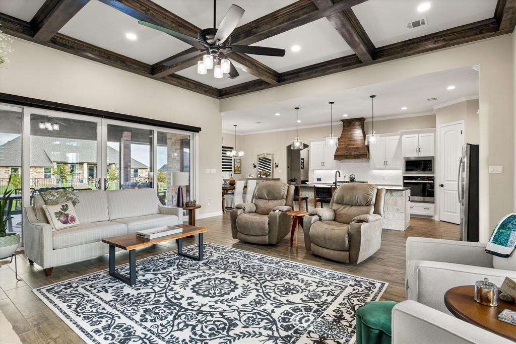 Living area featuring a coffered ceiling with wood beams, recessed lighting, and wood-finish flooring, complemented by a kitchen equipped with built-in cabinetry and a stone-clad island