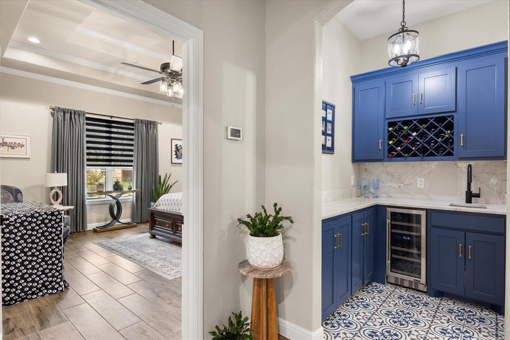 Wet bar featuring custom blue shaker cabinetry, built-in wine rack, stone-finish countertops, decorative patterned tile flooring, and a stainless steel beverage refrigerator