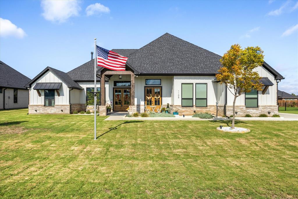 Modern farmhouse exterior featuring vertical board-and-batten siding, stone masonry accents, dual wood-framed entry doors, and dark metal roof detailing