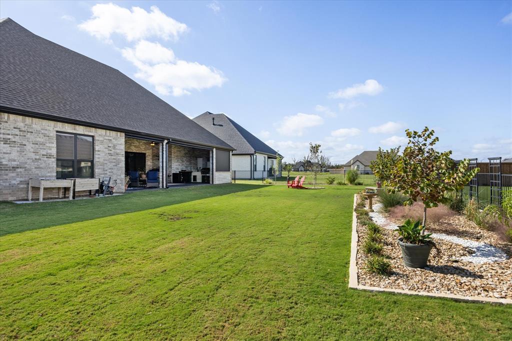 Rear exterior featuring a brick facade, covered patio, manicured lawn, and landscape bed with stone borders