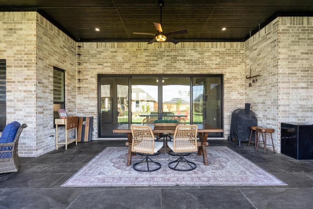Covered patio featuring brick masonry walls, dark-toned ceiling with recessed lighting, integrated ceiling fan, and large-format stone floor tiles