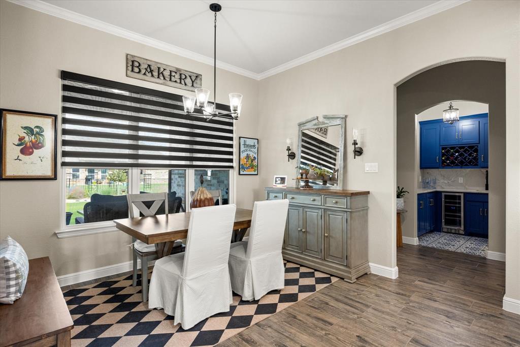 Dining area featuring wood-finish flooring, a contemporary multi-light chandelier, and a large window with dual-tone roller shades