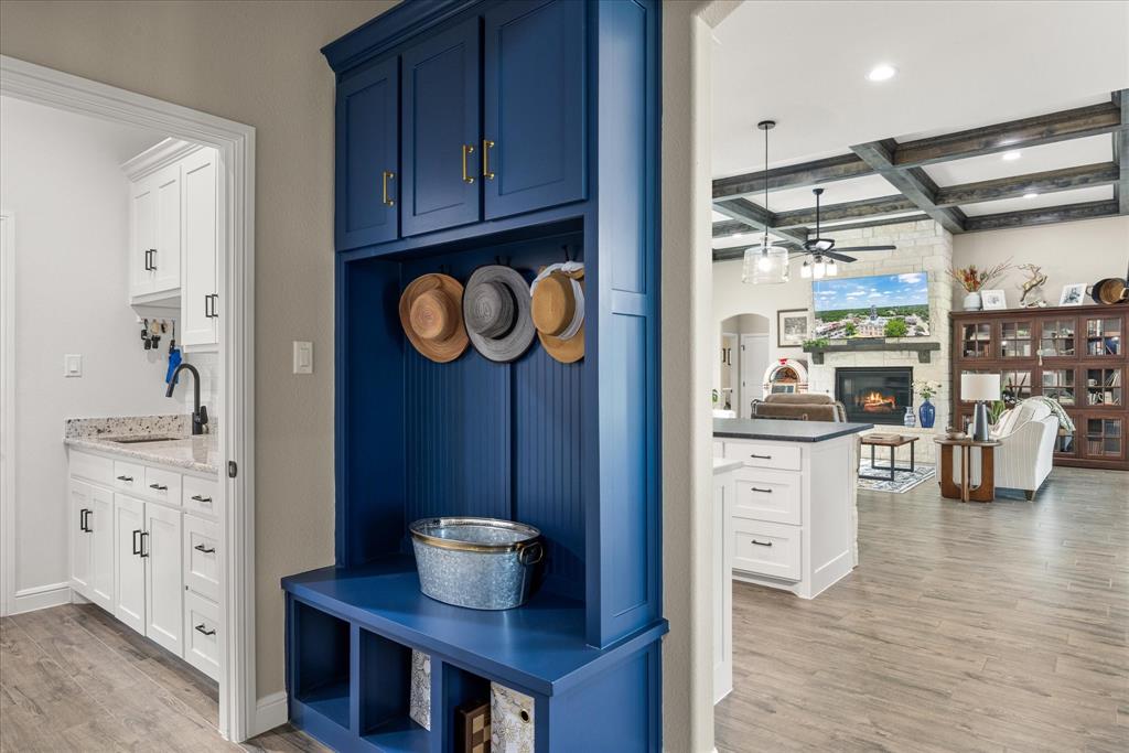 Built-in blue storage cabinetry with gold-toned hardware, wood-finish flooring, custom ceiling beams, and stone-surround fireplace
