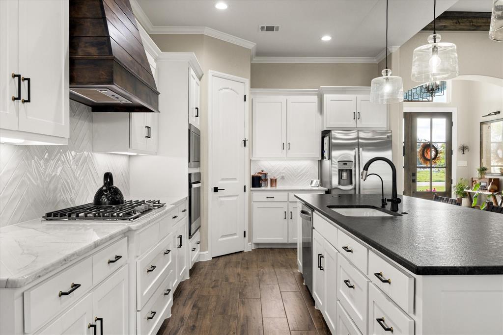 Kitchen featuring custom white cabinetry, a dark-toned wood-finish hood range, a large center island with a dark countertop, white herringbone-patterned backsplash, and wood-finish flooring