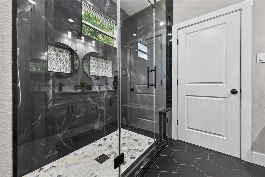 Primary bathroom offers an oversized walk-in shower with striking floor to ceiling marbled tile, frameless glass enclosure, built in shower bench and tiled flooring.