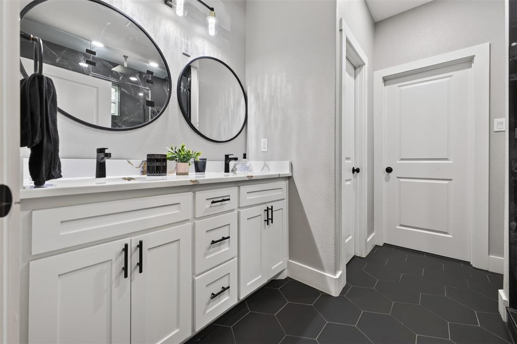 Primary Bathroom with double sink vanity with white cabinetry, plenty of storage, sleek black fixtures, and custom tile flooring.