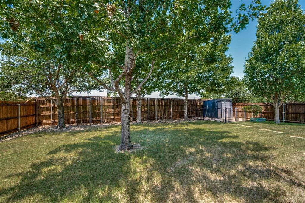 Private backyard featuring a sprawling lawn, mature trees, wood privacy fencing, and a detached storage structure