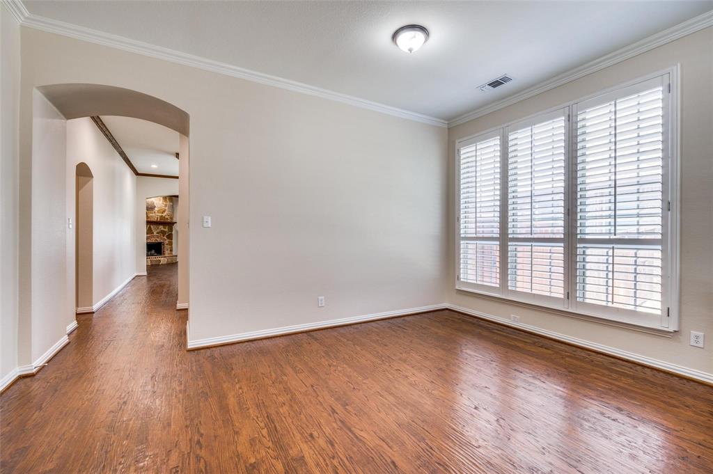 Room featuring wood-finish flooring, crown molding, multi-panel window with plantation shutters, and an arched entryway