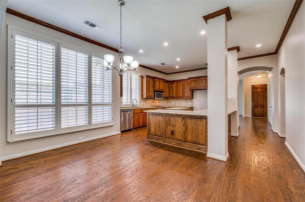 Wood-finish flooring, plantation shutters, crown molding, wood cabinetry, and a multi-light chandelier