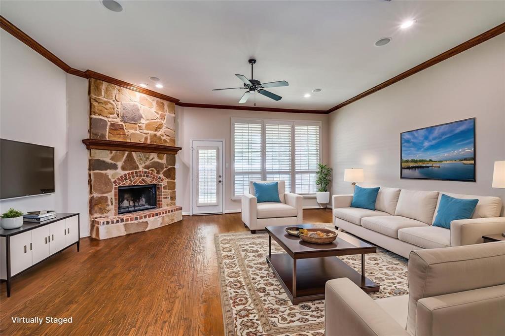 Living area featuring wood-finish flooring, full-height stone fireplace with a brick surround, crown molding, plantation shutters, and a ceiling fan
