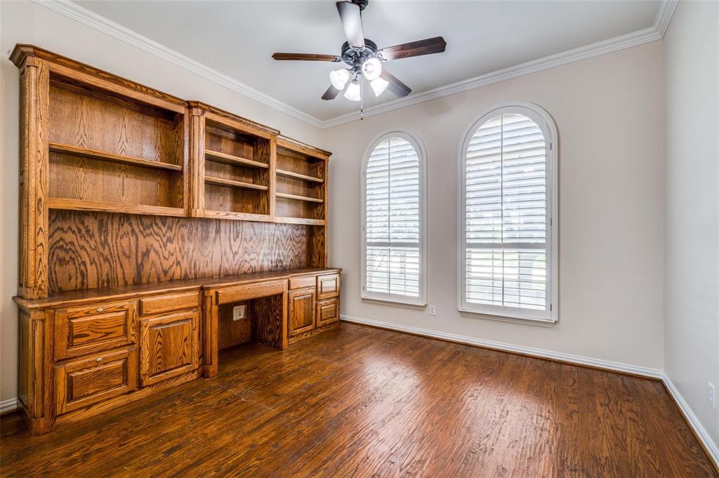 Custom built-in oak cabinetry with integrated shelving and desk workspace, arched windows with plantation shutters, wood-finish flooring, and crown molding