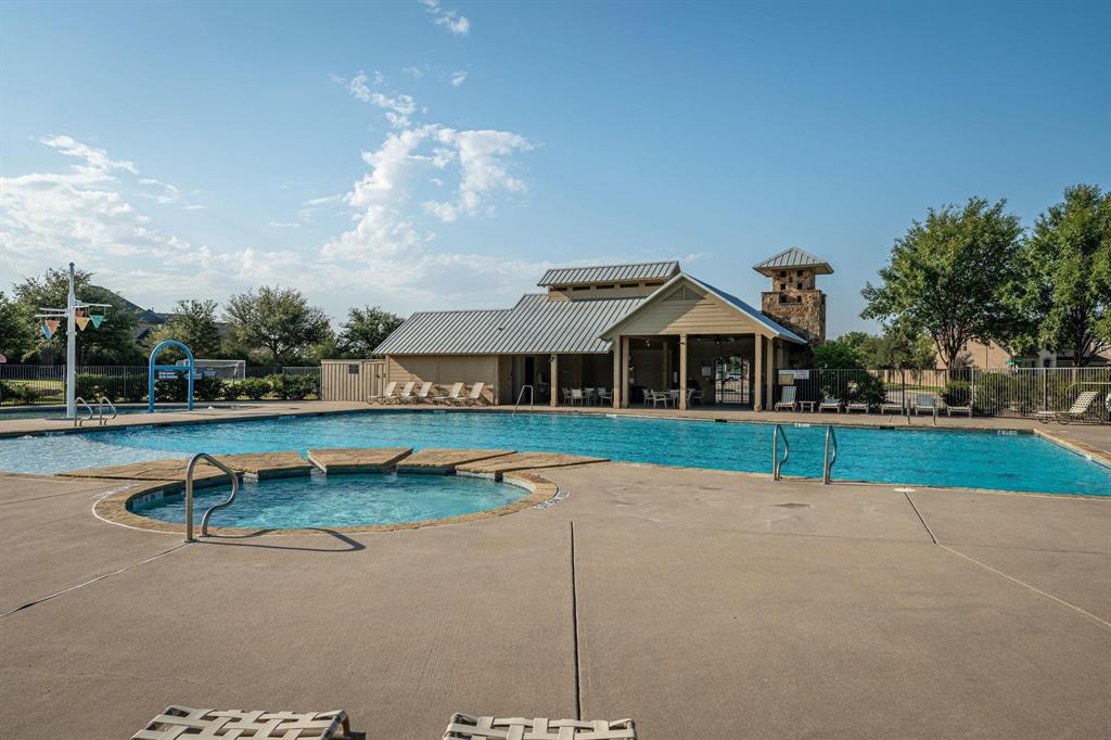 Swimming pool complex featuring a splash pad, circular spa, expansive concrete decking, and a covered clubhouse pavilion with stone accents