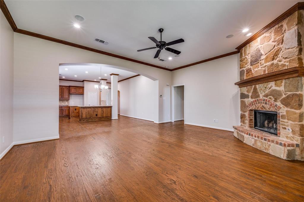 Living area featuring wood-finish flooring, crown molding, and a floor-to-ceiling stone fireplace with a brick surround