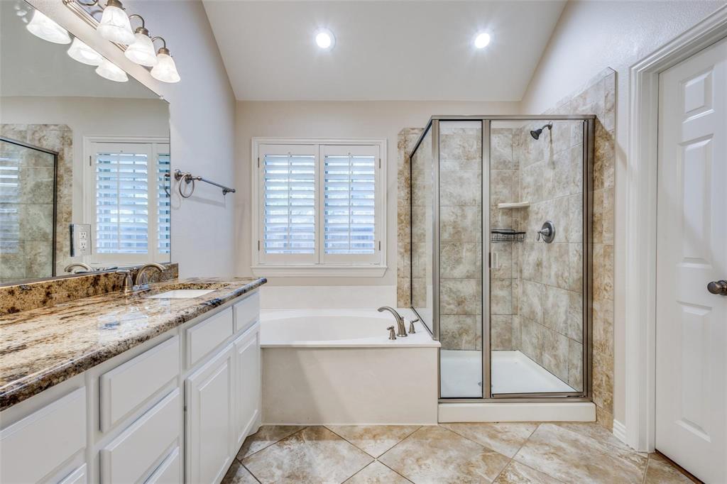 Bathroom featuring a white cabinetry vanity with a stone countertop, a deep soaking tub, and a glass-enclosed shower with tiled walls and flooring