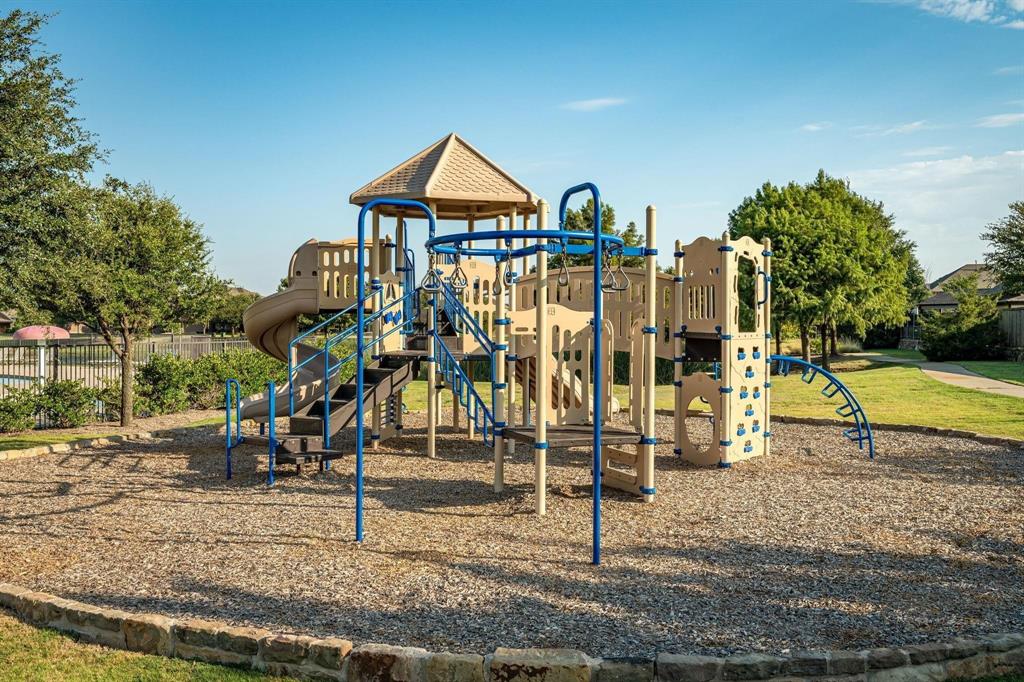 Recreational playground featuring a multi-level structure with slides, climbing walls, overhead bars, and a covered canopy, situated on a stone-bordered gravel ground cover