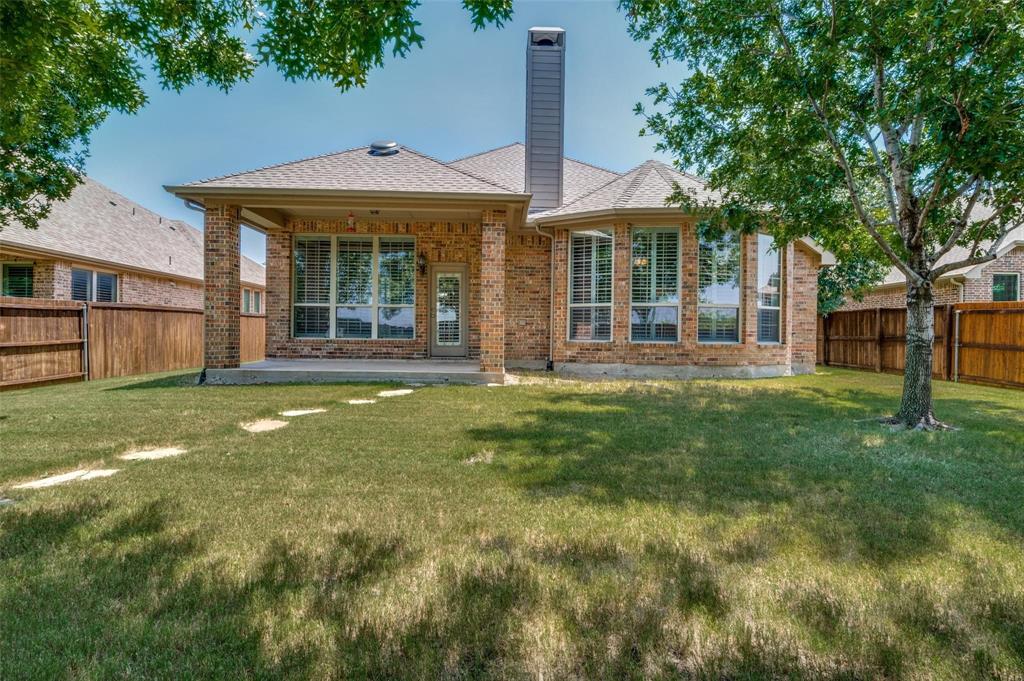 Brick exterior featuring a covered patio, tall chimney, expansive windows with grid detailing, and a fenced backyard with stone pavers