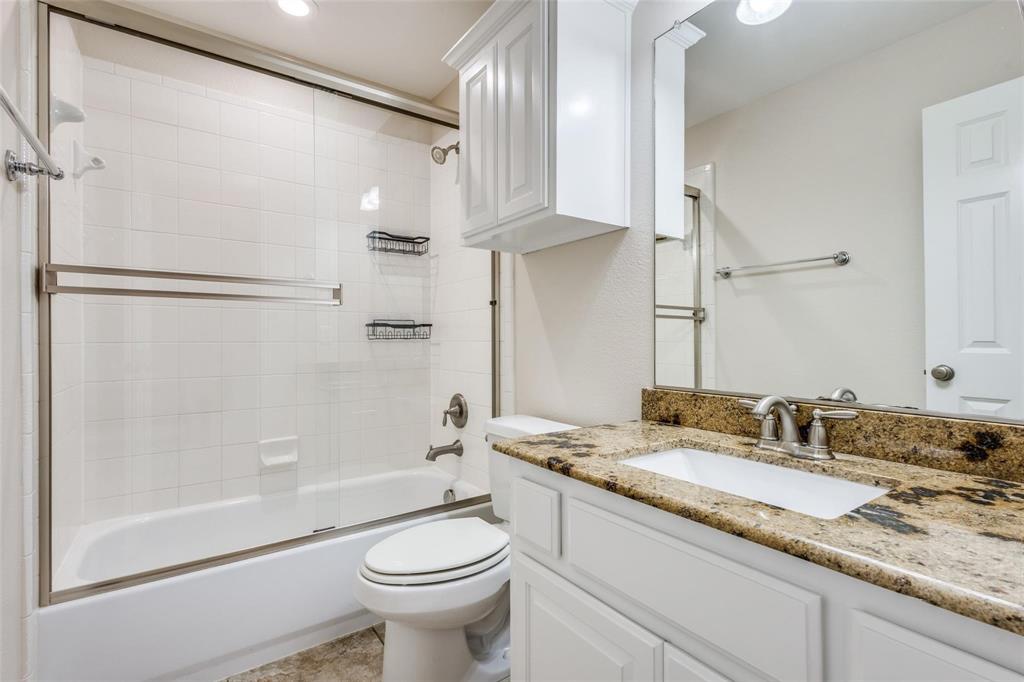 Bathroom featuring a granite-topped vanity with an integrated basin, white shaker-style cabinetry, a wall-mounted storage cabinet, and a tiled tub-shower combination with a sliding glass enclosure