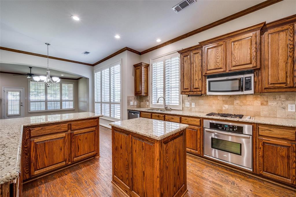 Kitchen featuring wood cabinetry, stone countertops, stainless steel appliances, wood-finish flooring, and plantation shutters