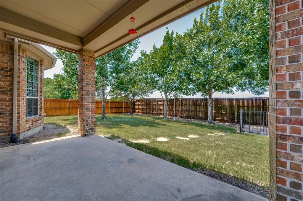 Covered concrete patio featuring brick structural pillars, enclosed by a wood privacy fence and mature trees