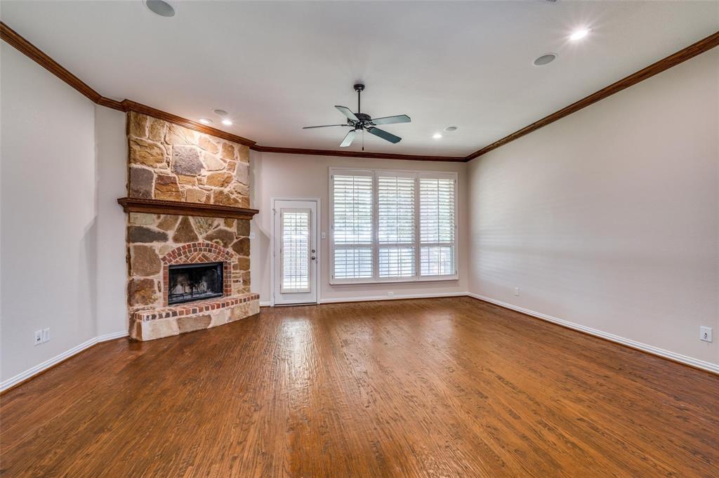 Living area featuring wood-finish flooring, a floor-to-ceiling stone fireplace with a brick hearth, crown molding, a ceiling fan, and large windows with plantation shutters